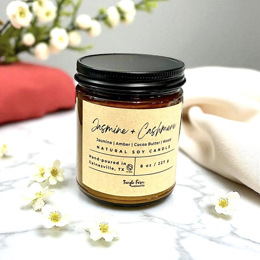 8oz Jasmine and Cashmere soy candle, infused with cocoa butter cashmere fragrance, presented in an amber jar topped with a gold metal lid.