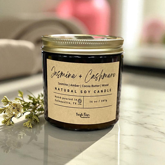 14oz Jasmine and Cashmere soy candle, infused with cocoa butter cashmere fragrance, presented in an amber jar topped with a gold metal lid.