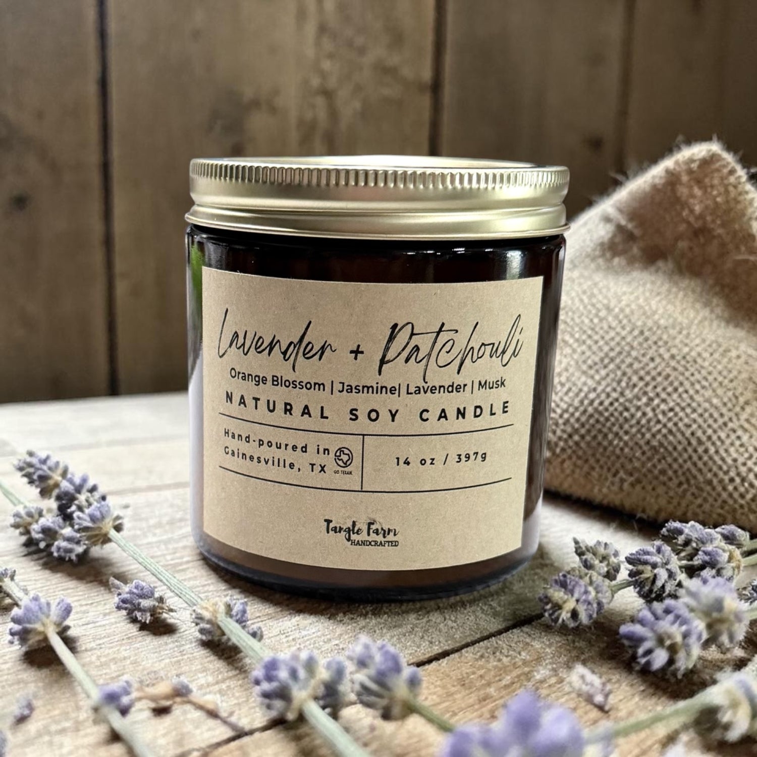 Natural soy candle with lavender and patchouli scent on a wooden surface with lavender flowers.
