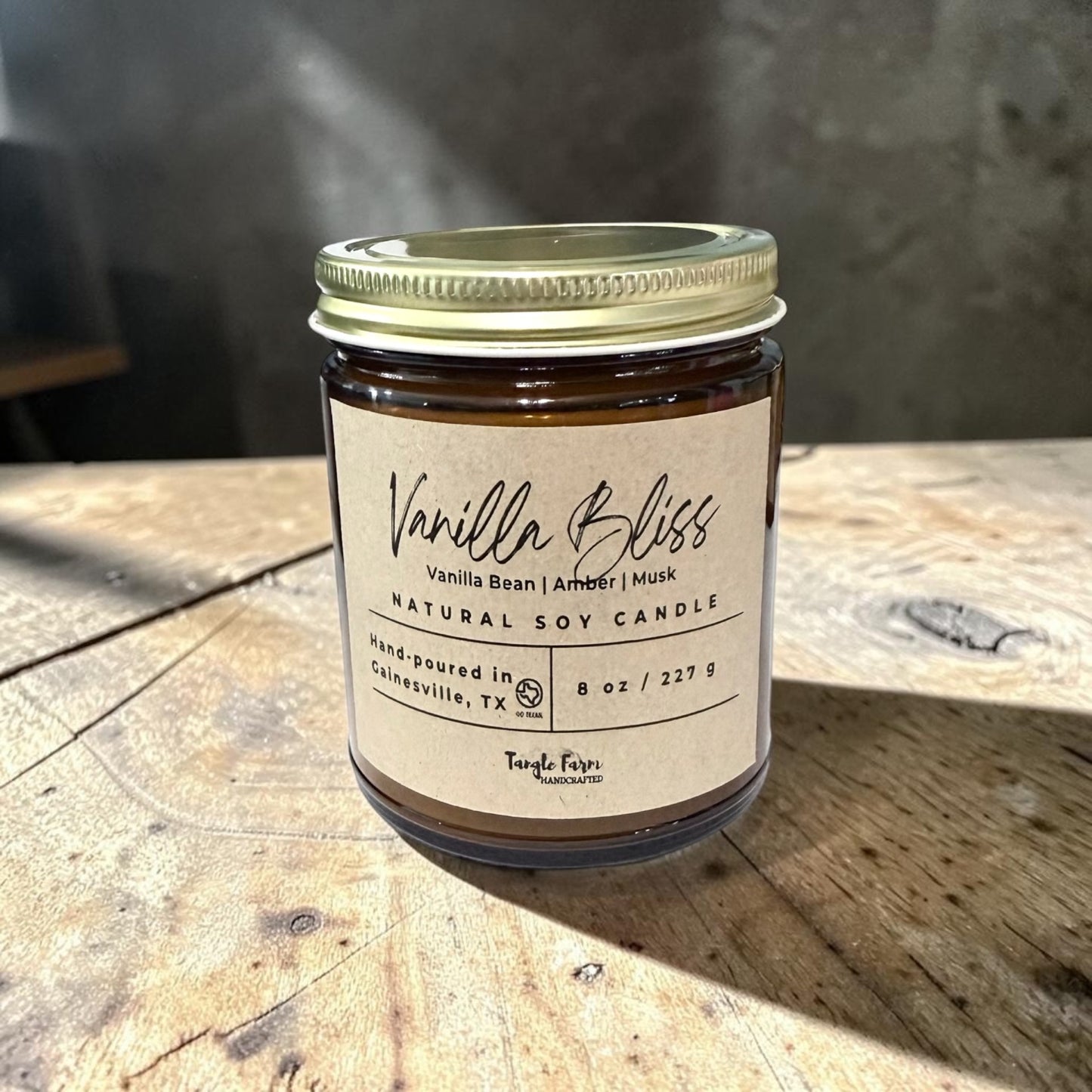 Vanilla Bliss candle jar on a wooden surface with a blurred background