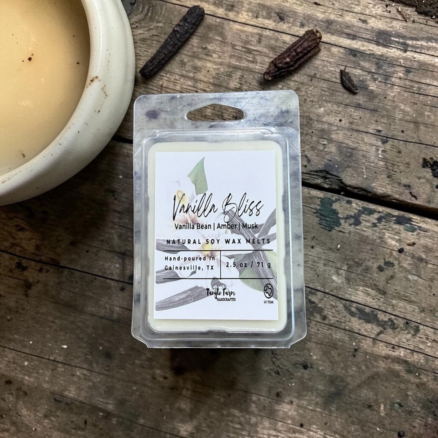 Vanilla Bliss wax melt package on a wooden surface with a candle and vanilla beans.