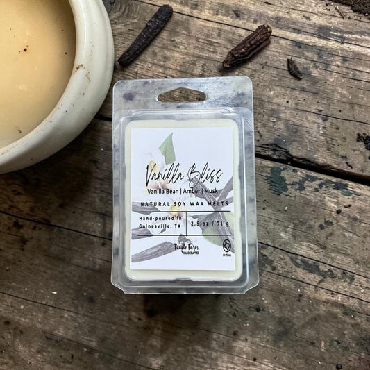 Vanilla Bliss wax melt package on a wooden surface with a candle and vanilla beans.